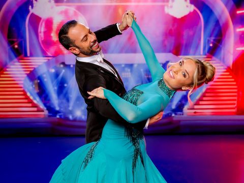 Ein Paar in eleganter Tanzpose auf einer Bühne mit buntem Hintergrund und Treppen