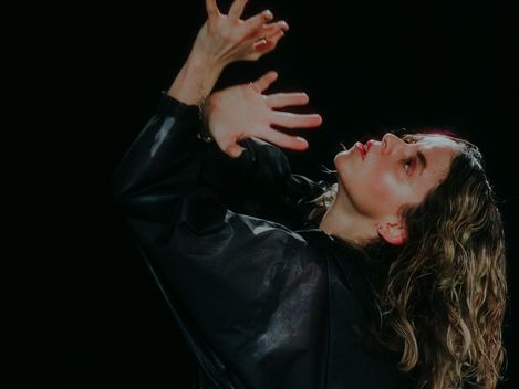 Woman with curly hair wearing a black top raising her hands in front of her face and looking upward