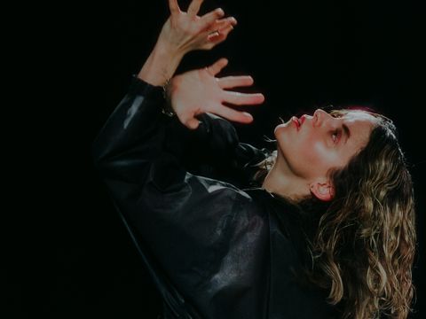 Woman with curly hair wearing a black top raising her hands in front of her face and looking upward