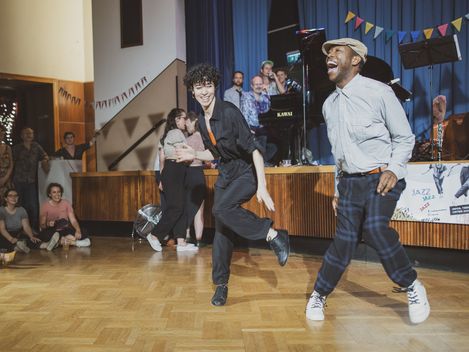 Two people dancing in a hall with an audience in the background