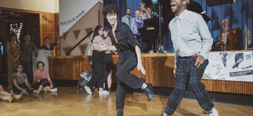 Zwei tanzende Personen in einem Saal mit Publikum im Hintergrund