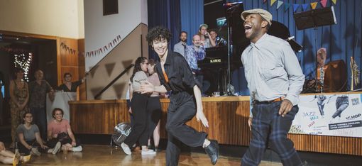 Two people dancing in a hall with an audience in the background