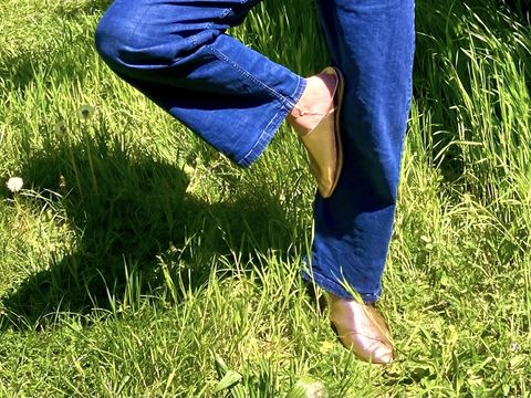 Legs in blue jeans and brown shoes standing on green grass with one leg bent