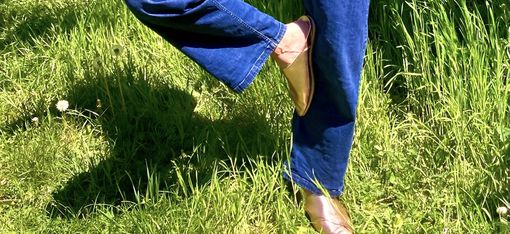 Legs in blue jeans and brown shoes standing on green grass with one leg bent