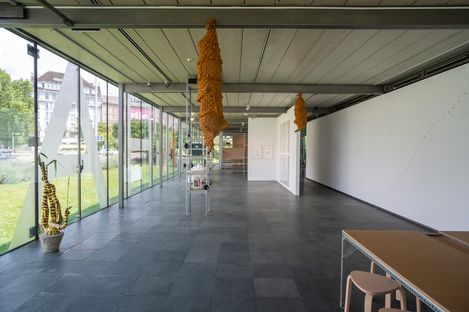 Large bright exhibition space with glass front, several hanging and standing sculptures made of organic material, and modern furnishings.