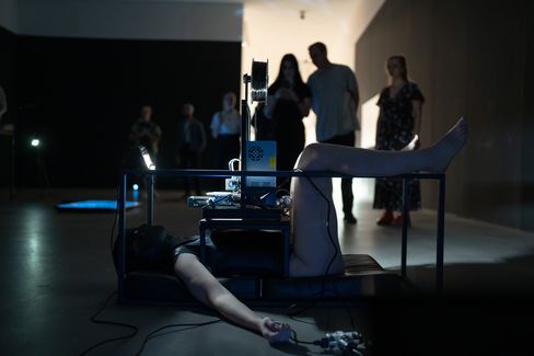Two people kneel on opposite sides of illuminated surfaces with metal rods and apparatuses in a dark room with a large arch in the background.