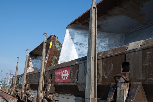 Several rusty open freight train cars with a red logo on the side under a blue sky.