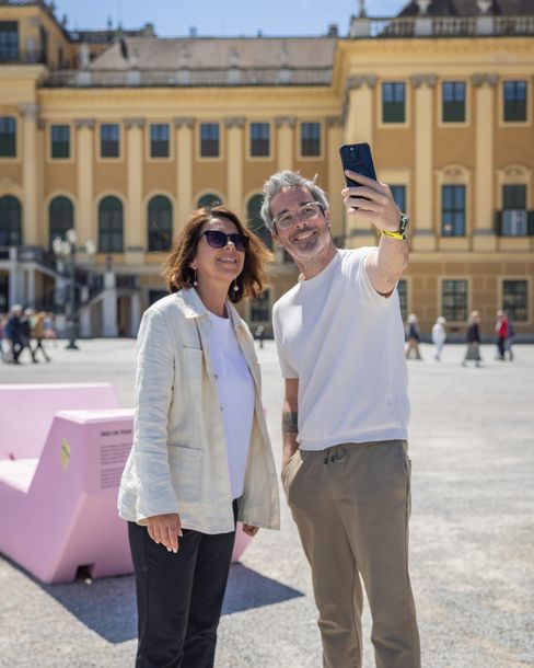 Zwei Besucher machen ein Selfie vor Schloss Schönbrunn neben einem rosa Enzi-Sitzmöbel.