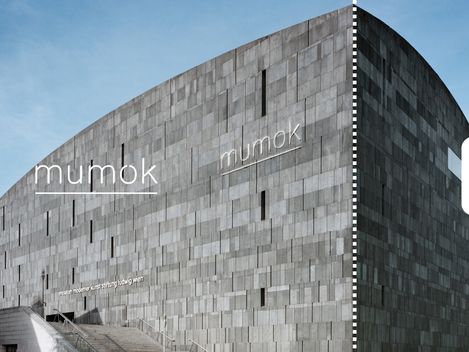 Frontalaufnahme der grauen Fassade des mumok vor blauem Himmel.