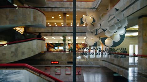 Interior of a multi-level building with staircases and a glass wall displaying exhibition text.