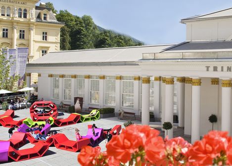 Bunte Enzos Sitzmöbel im Außenbereich vor dem historischen Trinkhalle-Gebäude in Bad Ischl, Menschen liegen und sitzen auf den modularen Elementen.