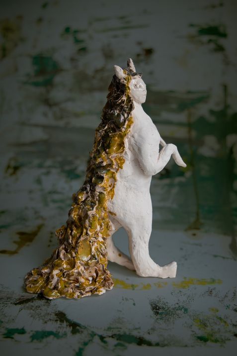 Sculpture of an upright standing animal with a long irregularly shaped tail and small horns.