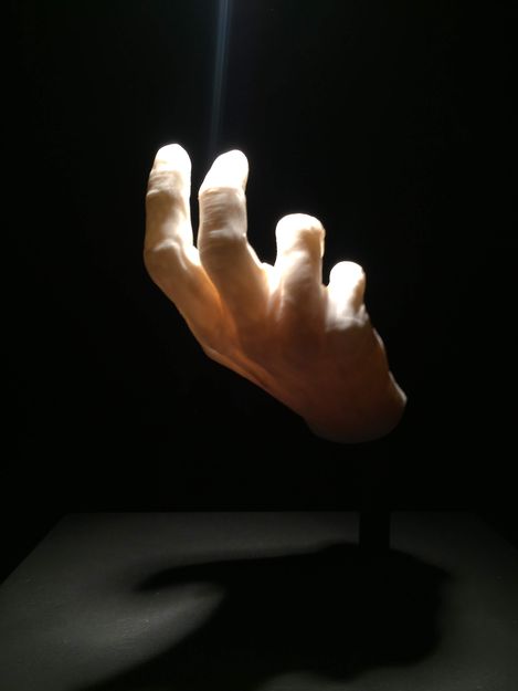 A single hand with spread fingers reaching upward into a beam of light against a black background.