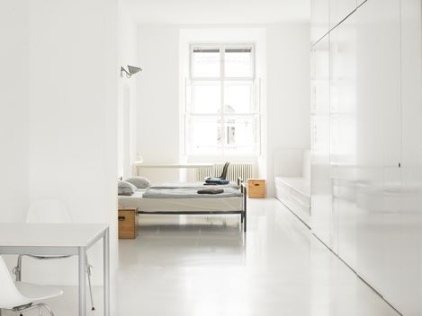 Minimalist bedroom with white desk, chair, bed in front of window, and large white wardrobe.
