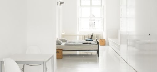 Minimalist bedroom with white desk, chair, bed in front of window, and large white wardrobe.
