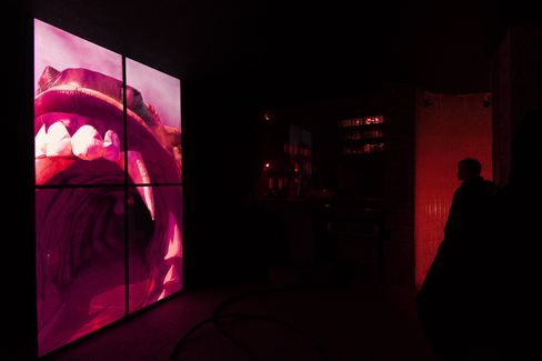 Large illuminated image of an open mouth showing teeth in a dark room.