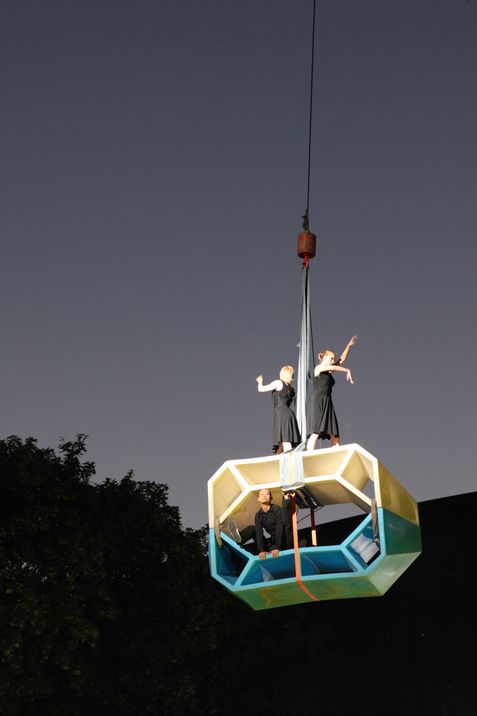 Dancers stand on Enzos in various colors arranged and lifted in front of the historic baroque façade of MuseumsQuartier in the evening light.