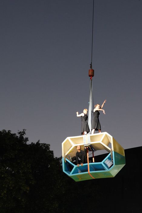 Dancers stand on Enzos in various colors arranged and lifted in front of the historic baroque façade of MuseumsQuartier in the evening light.