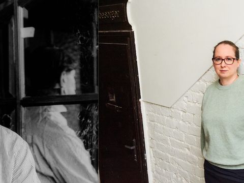 Two people, one in black-and-white facing forward and the other in color standing sideways against a white brick wall