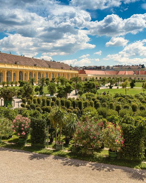 Historische Gartenanlage und Orangerie im Schlosspark Schönbrunn in Wien unter blauem Himmel.