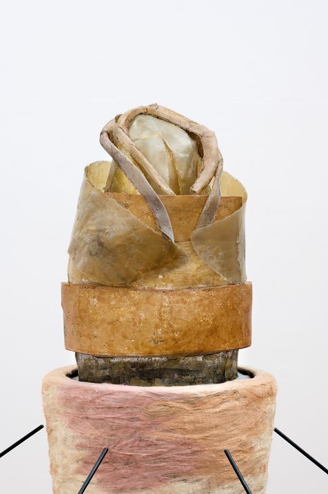 Sculpture made of organic material with a wrapped, leaf-like shape on a round base with three thin rods
