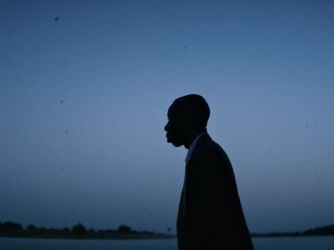 Silhouette eines Mannes im Profil vor einem dunklen Himmel und Gewässer im Hintergrund