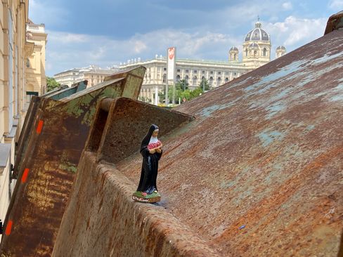 Small nun figurine stands on rusty metal surface with historic building in the background.