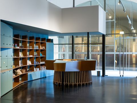 Cash desk and shop area in MQ Freiraum featuring a central round wooden counter, open shelves with books and design objects, and a large glass façade.