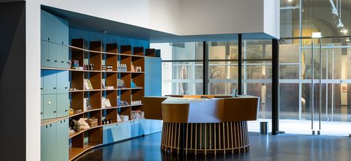 Cash desk and shop area in MQ Freiraum featuring a central round wooden counter, open shelves with books and design objects, and a large glass façade.