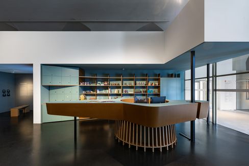 Cash desk with integrated shop in MQ Freiraum, modern architecture with blue-green shelving, wooden counter, and a view into the adjacent exhibition space.