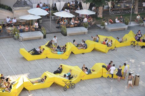 Yellow Enzi seating at MuseumsQuartier Vienna, people relaxing in the sun near the café terrace.