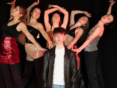 Fünf junge Frauen stehen in einer Choreografie hinter einem jungen Mann.