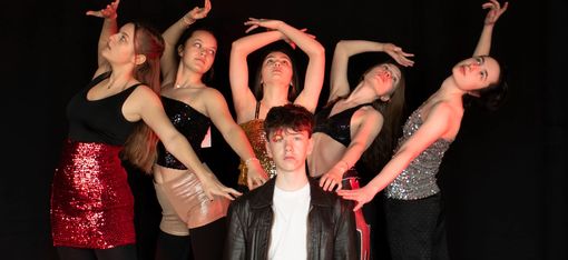 Five young women are standing behind a young man as part of a choreographed routine.