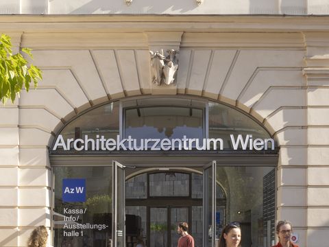Four people on their way to or from the main entrance of the Architekturzentrum Wien, which has a large door with a round-arched window above which the words “Architekturzentrum Wien” are displayed.