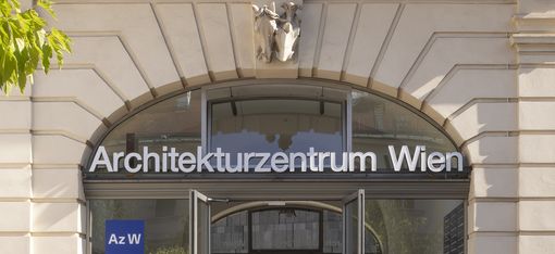 Four people on their way to or from the main entrance of the Architekturzentrum Wien, which has a large door with a round-arched window above which the words “Architekturzentrum Wien” are displayed.