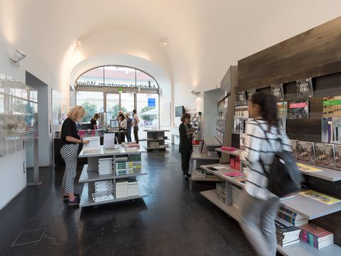 A room with a vaulted ceiling and many shelves and tables with books on them. Some people are looking at books.