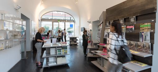 A room with a vaulted ceiling and many shelves and tables with books on them. Some people are looking at books.