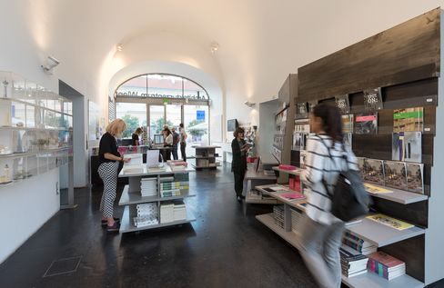 A room with a vaulted ceiling and many shelves and tables with books on them. Some people are looking at books.