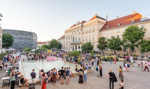 Menschenmenge an einem großen rechteckigen Wasserbecken vor historischen Gebäuden bei Tageslicht