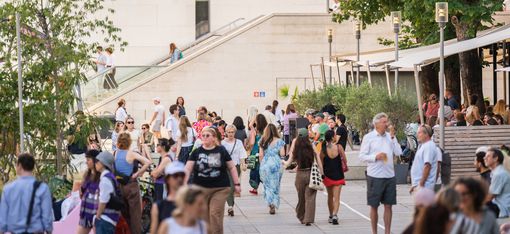 Crowd of people on a plaza in front of a modern building with stairs and trees