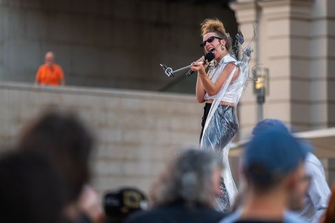 Woman with updo hairstyle and sunglasses sings in front of a crowd