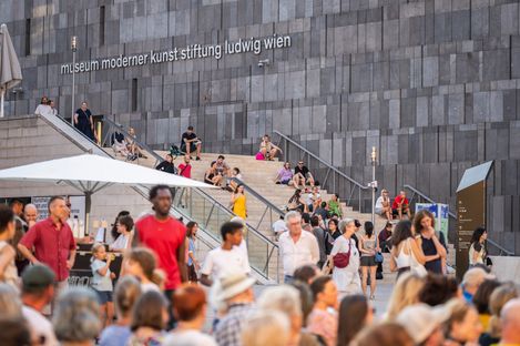 Menschenmenge vor und auf einer großen Treppe mit der Aufschrift 'museum moderner kunst stiftung ludwig wien' an einer modernen Steinwand
