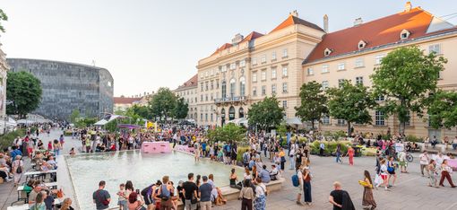 Menschenmenge an einem großen rechteckigen Wasserbecken vor historischen Gebäuden bei Tageslicht