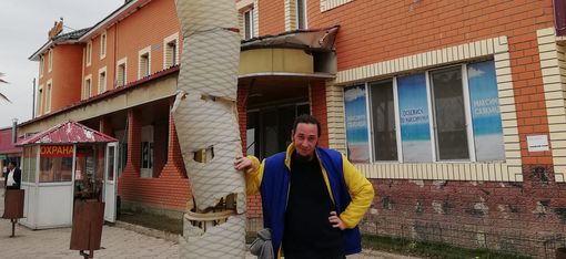 Person leaning against a streetlight with an artificial palm tree in front of a multi-story brick building with large windows.