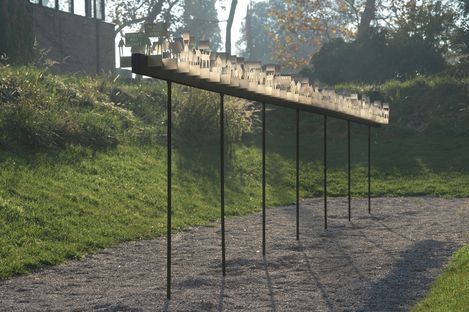 Long narrow installation with translucent figures on thin poles outdoors on a gravel path.