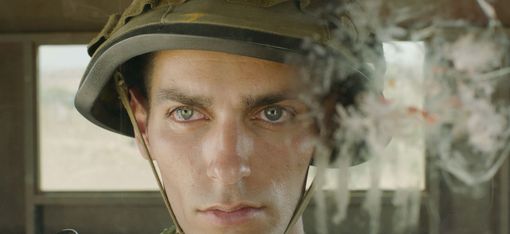 A film still with a close-up of a face wearing a military helmet in a lookout post.