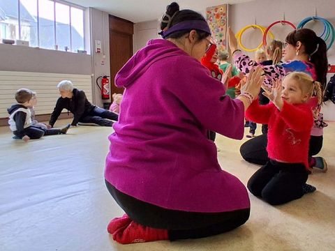 Mehrere Kinder und Erwachsene sitzen auf dem Boden eines hellen Raums und klatschen sich gegenseitig in die Hände
