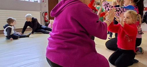 Mehrere Kinder und Erwachsene sitzen auf dem Boden eines hellen Raums und klatschen sich gegenseitig in die Hände