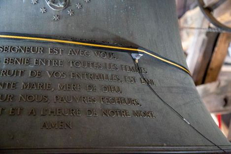Nahaufnahme eines großen Metallglockenkörpers mit französischer Inschrift und einem daran befestigten Beschleunigungssensor.