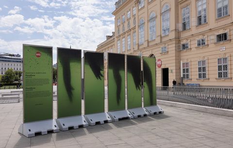 Several green panels with underwater-like silhouettes form an outdoor art installation in front of a large building.